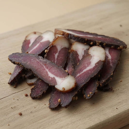 Whole biltong piece being sliced by hand, showing the rich texture and traditional South African biltong cut