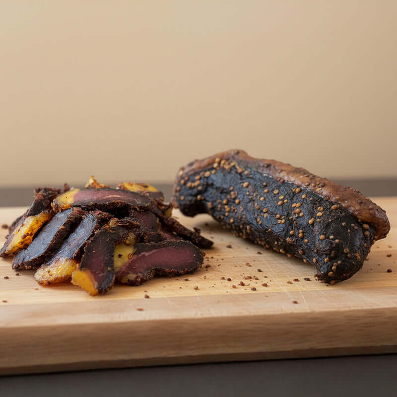 Pile of sliced geelvet biltong next to a whole piece, clearly showing the distinctive yellow fat and lean meat contrast of authentic South African biltong.