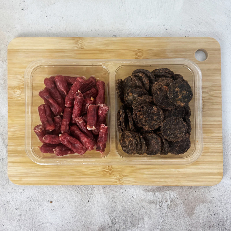 oubaas snack pack on a board in an plastic container that showcase the brand and weight of 400g. This is salami bites and chutney wheels and image without the packaging showcasing what is inside