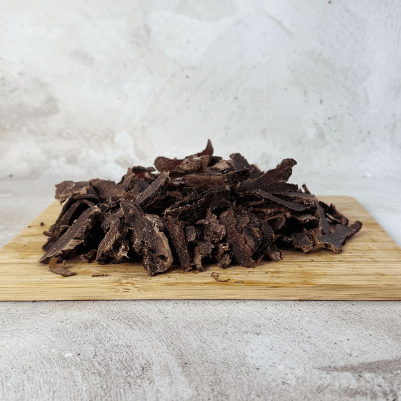 Dried springbok biltong on a wooden cutting board with a light gray background